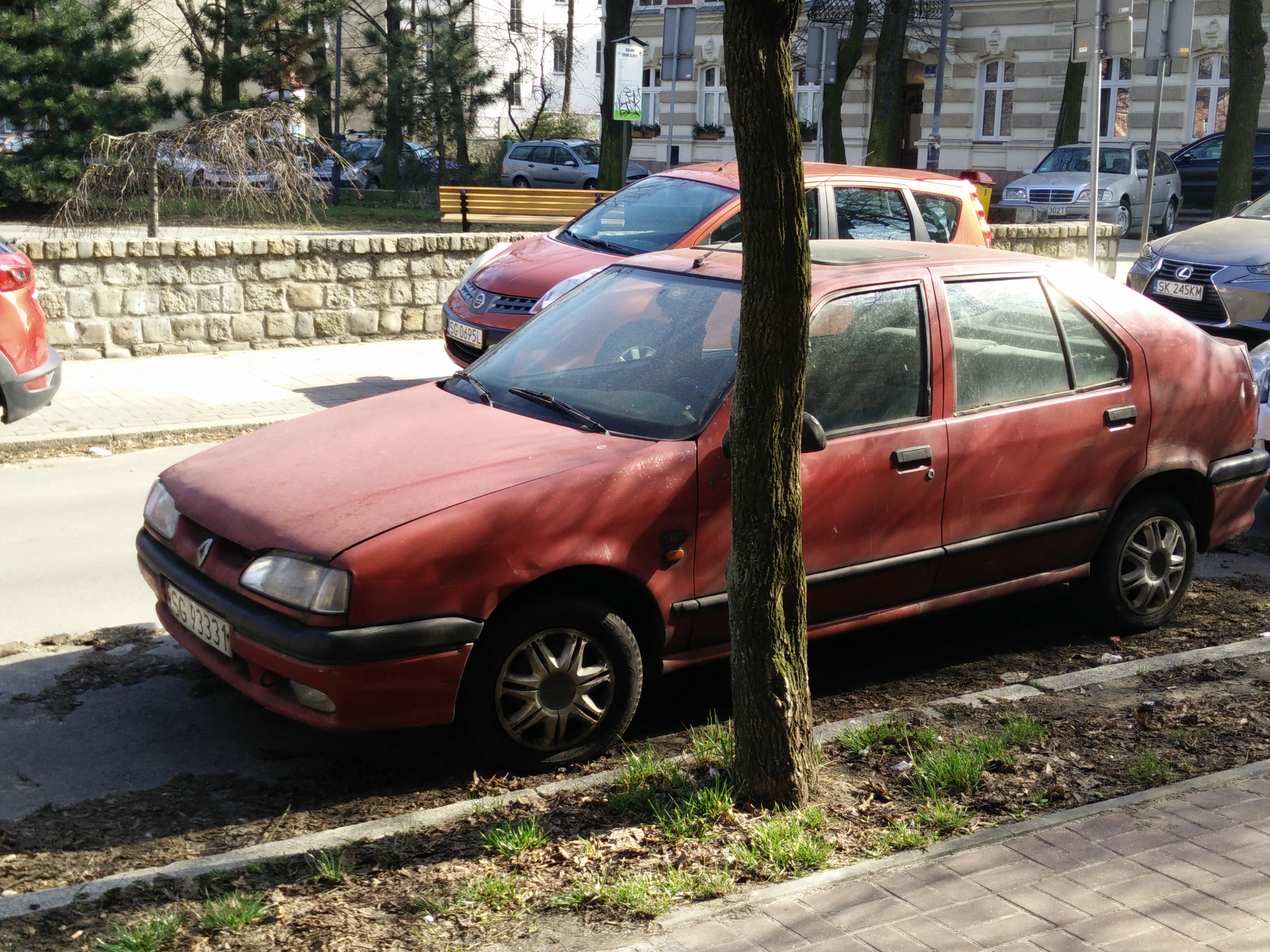 Red four door hatchback car, sadly obscured by a tree